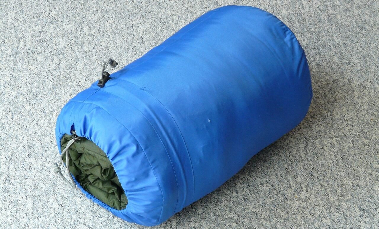 An image of a rolled-up sleeping bag, compact and secured with straps. The sleeping bag is made from durable, weather-resistant material, with a soft interior lining peeking out. It’s designed for easy transport, perfect for camping or outdoor use.